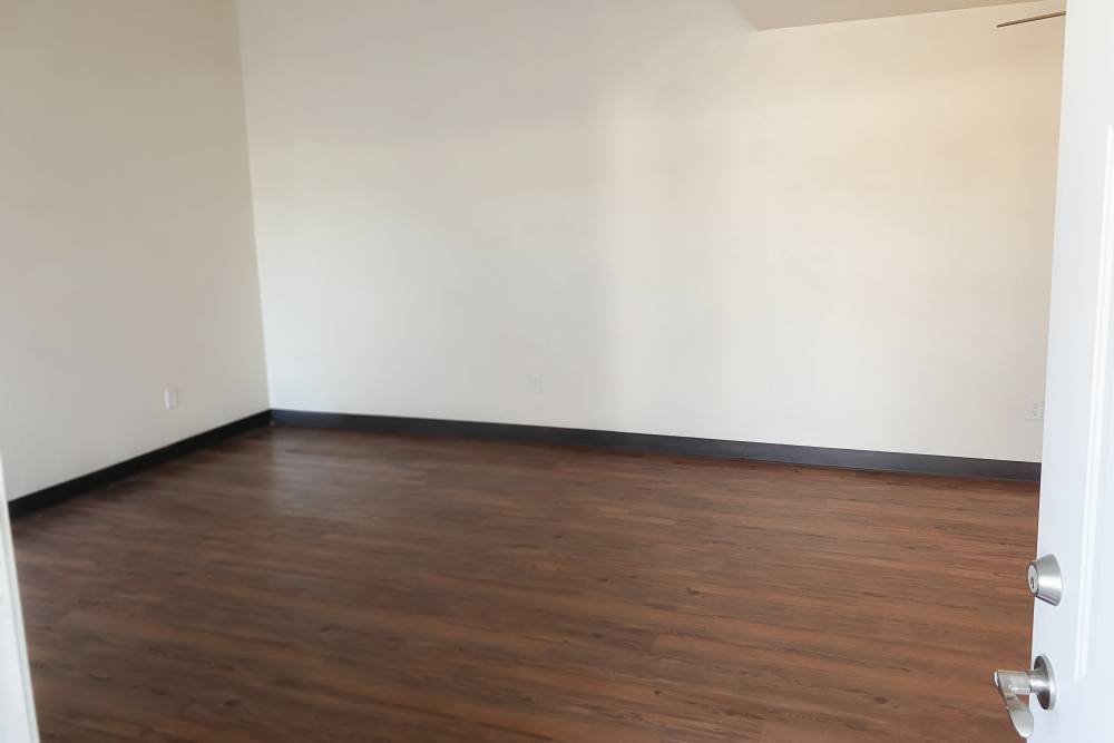 Bright living room with wood-style flooring at Perry Acres Apartments in New Haven, Michigan