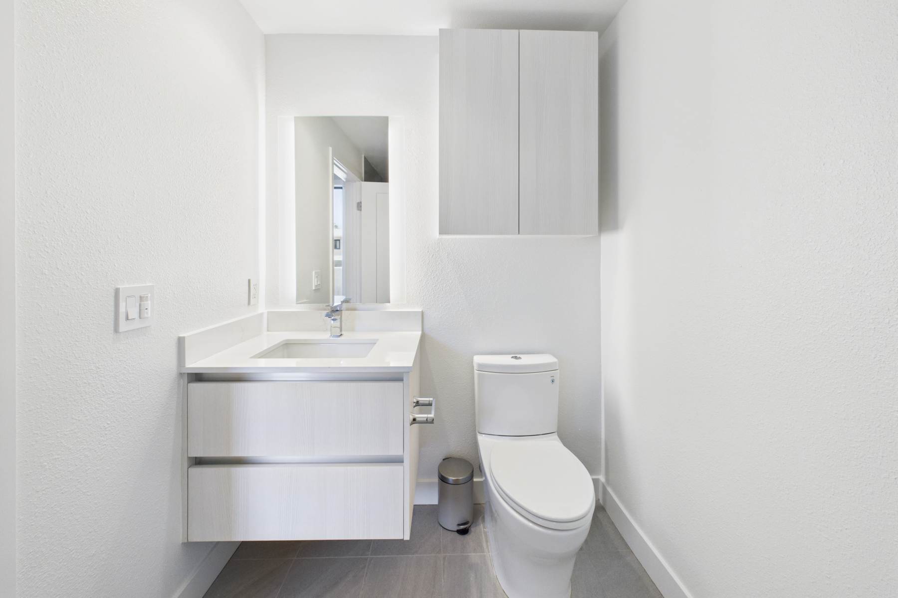 Minimalist bathroom with floating vanity, white toilet, wall cabinet, and large mirror with lighting at Luxe Villas in Brentwood, California 