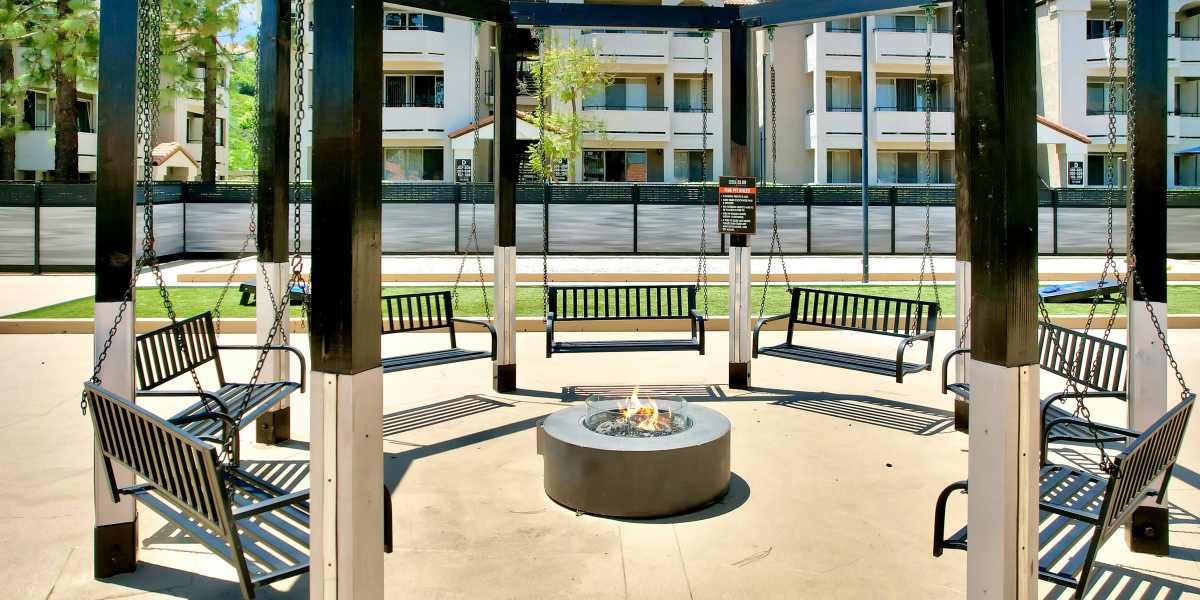 Fire pit surrounded by swing seating at Sierra Del Oro Apartments in Corona, California