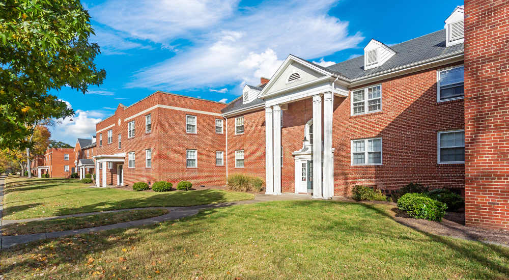 Exterior view of an apartment building surrounded by a well-maintained lawn and trees at Terraces at Bellevue in Richmond, Virginia