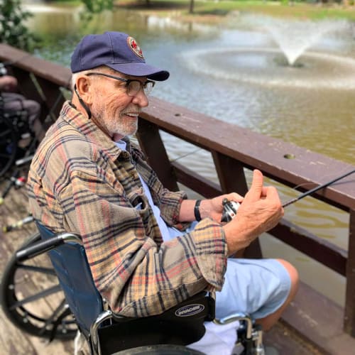 A Resident in a wheelchair sitting outside by a body of water at Oxford Glen Memory Care at Owasso in Owasso, Oklahoma
