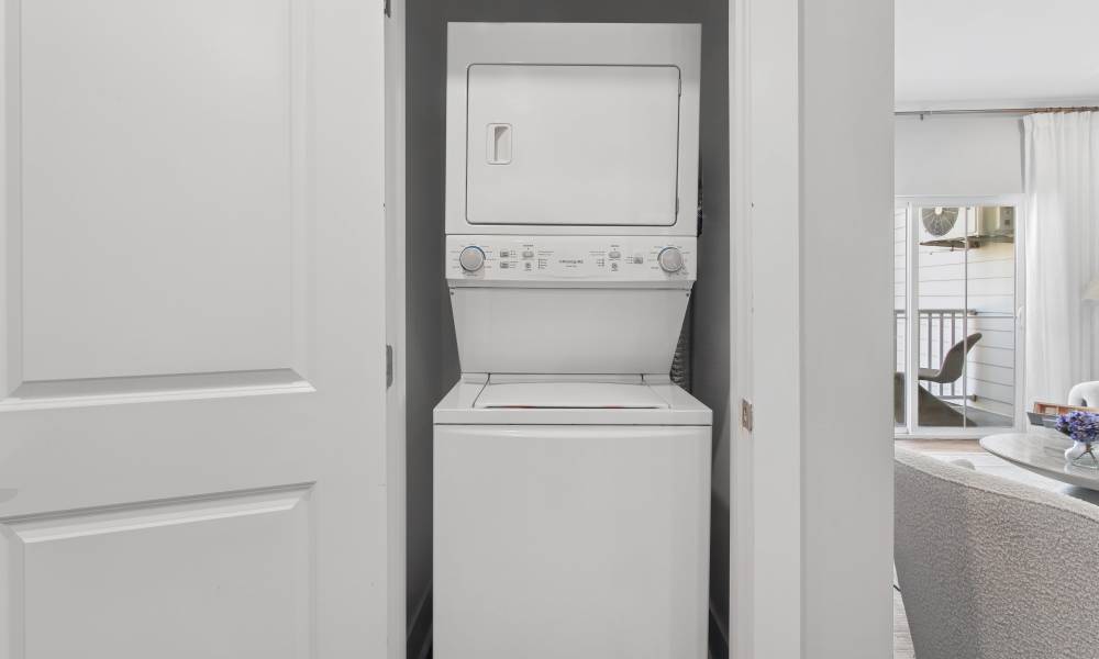 Stacked washer and dryer in laundry closet with open living area visible beyond at Everett at Port Wentworth in Port Wentworth, Georgia