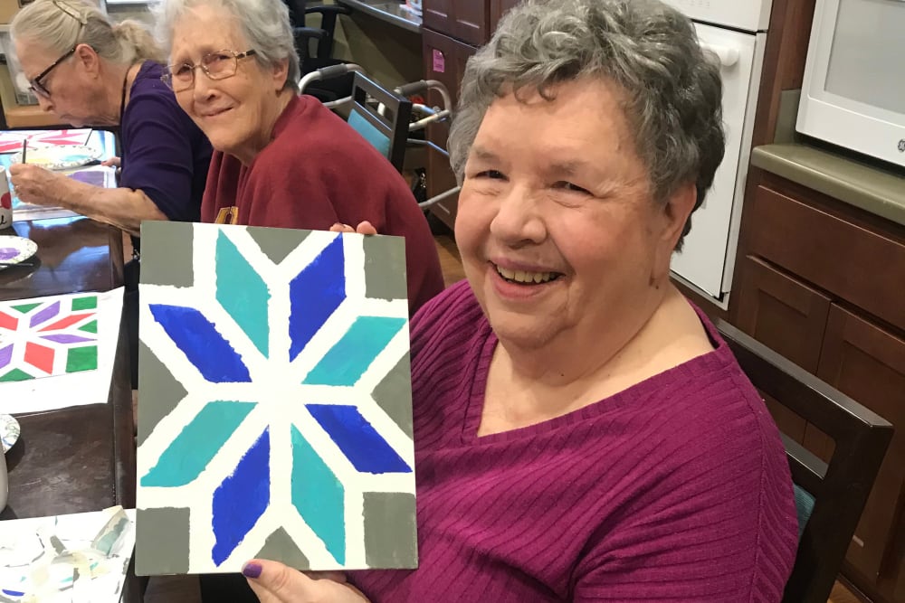 Resident smiling and showing her artwork at Edencrest at Riverwoods in Des Moines, Iowa