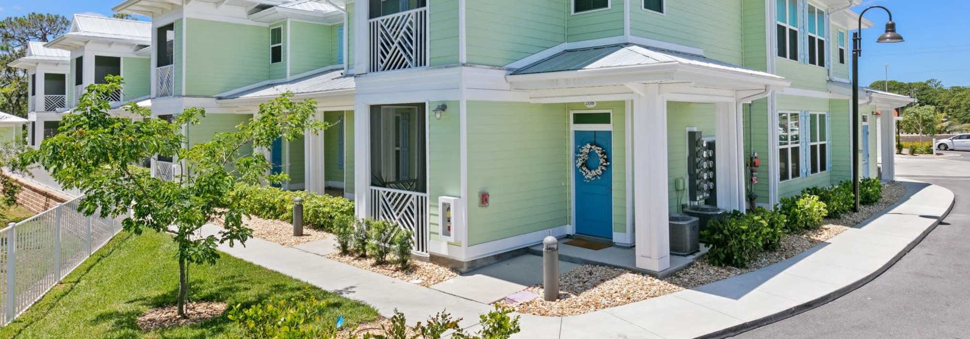Charming green facade with lush landscaping and a welcoming blue front door at Lemon Bay Apartments in Englewood, Florida.