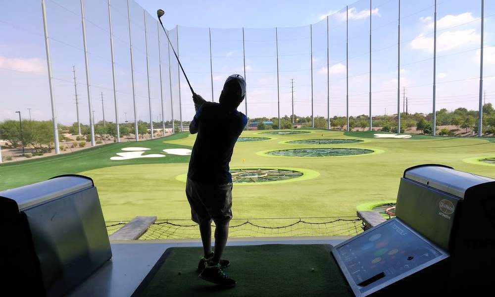 Golfer swinging club at driving range with green turf and target areas in background near The Havenly Gilbert in Gilbert, Arizona