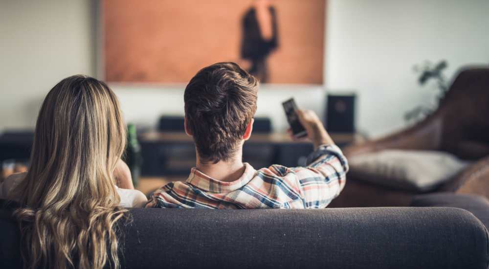 Resident couple watching TV in their apartment home at The Apartments At Kelton Station in Williamsburg, Virginia