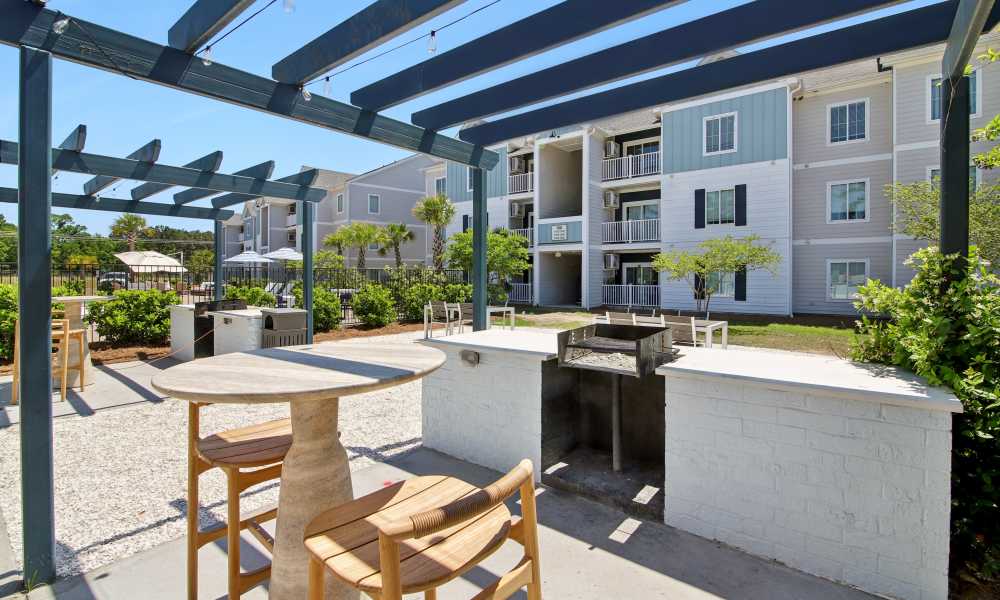 Outdoor grilling area with seating and shaded pergola near apartment buildings and landscaped greenery at Everett at Port Wentworth in Port Wentworth, Georgia