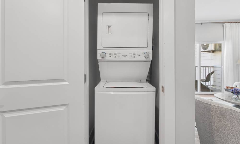 Stackable washer and dryer in a laundry closet with open living area visible beyond at Everett at Port Wentworth in Port Wentworth, Georgia