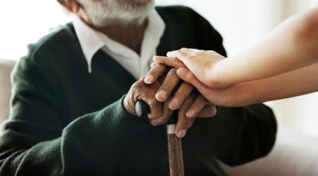 Resident resting his hands on a cane with caregiver's hands on top at Cascade Park Adult Day Health in Tacoma, Washington