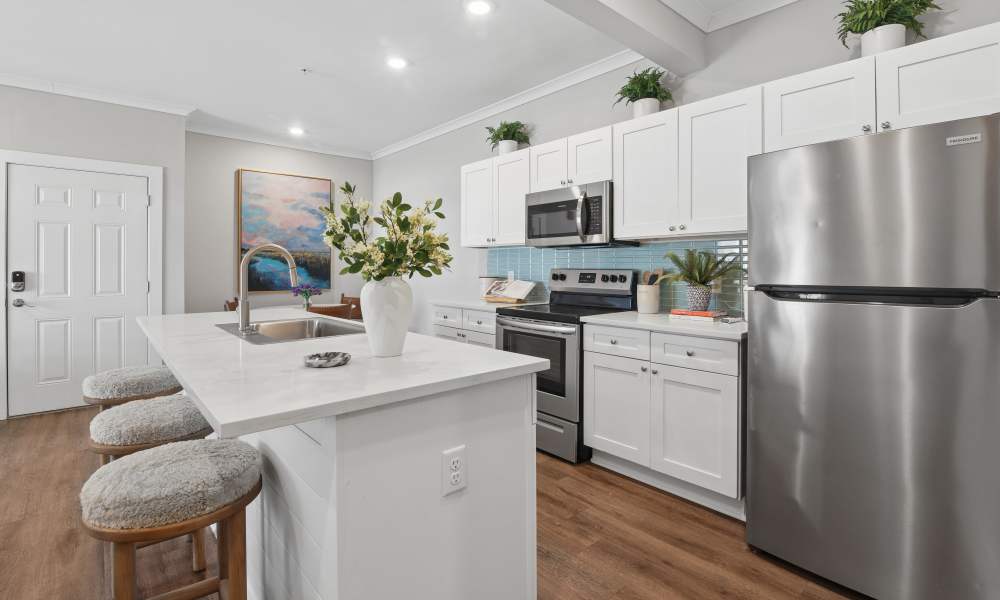 Modern apartment kitchen featuring white shaker cabinets, stainless steel appliances, a spacious kitchen island with bar seating, quartz countertops, and warm wood flooring.