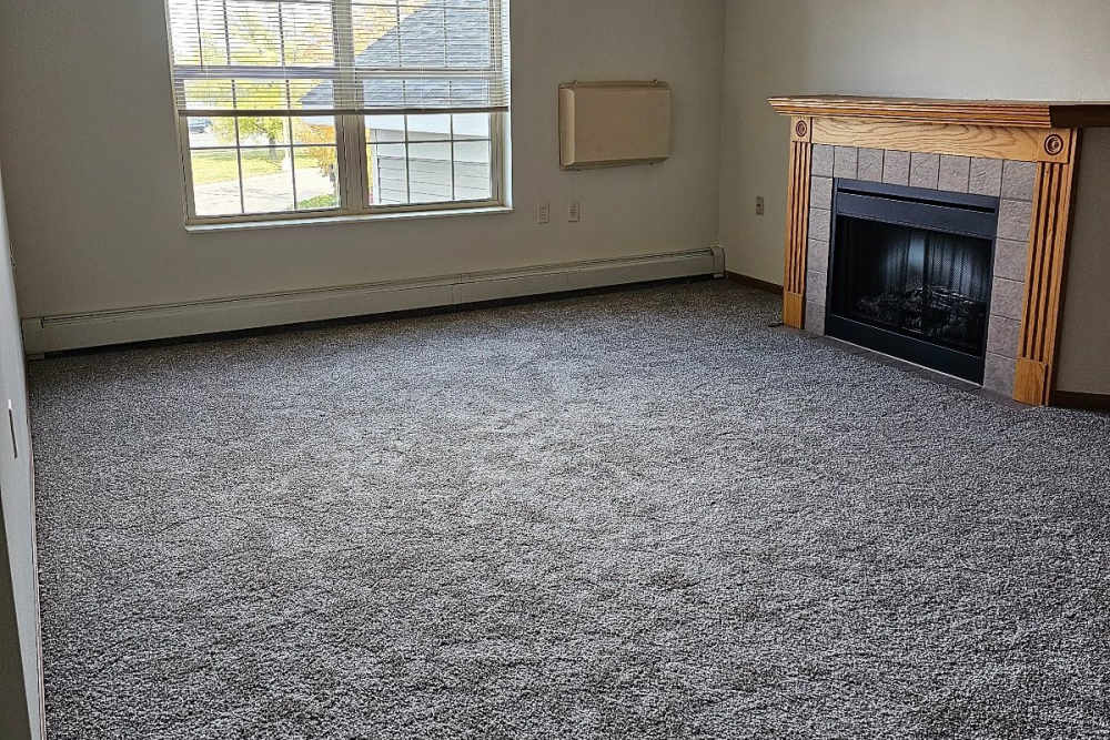 Spacious living room with fireplace, carpet flooring and large window at Westwood Parkway Estates in Saint Cloud, Minnesota