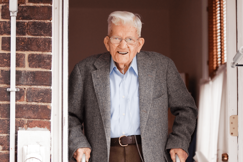 Resident walking out the front door of his home with a walker