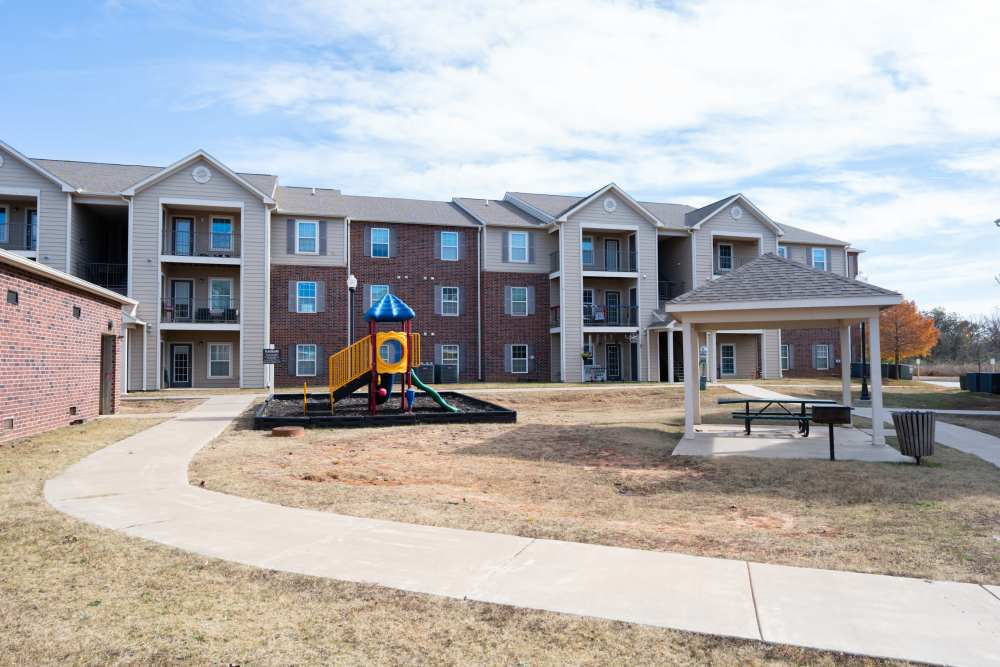 Family-friendly playground beside modern apartment buildings with shaded gazebo at Shawnee Park in Shawnee, Oklahoma