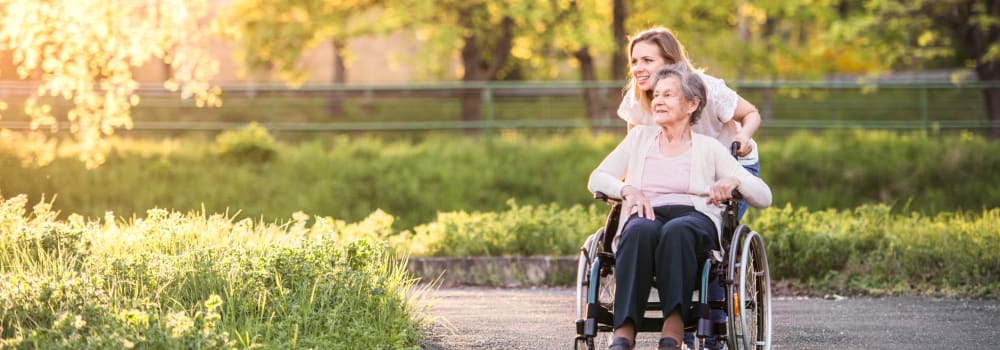 A friendly staff member pushing a resident in a wheel chair at a Stoney Brook community. 