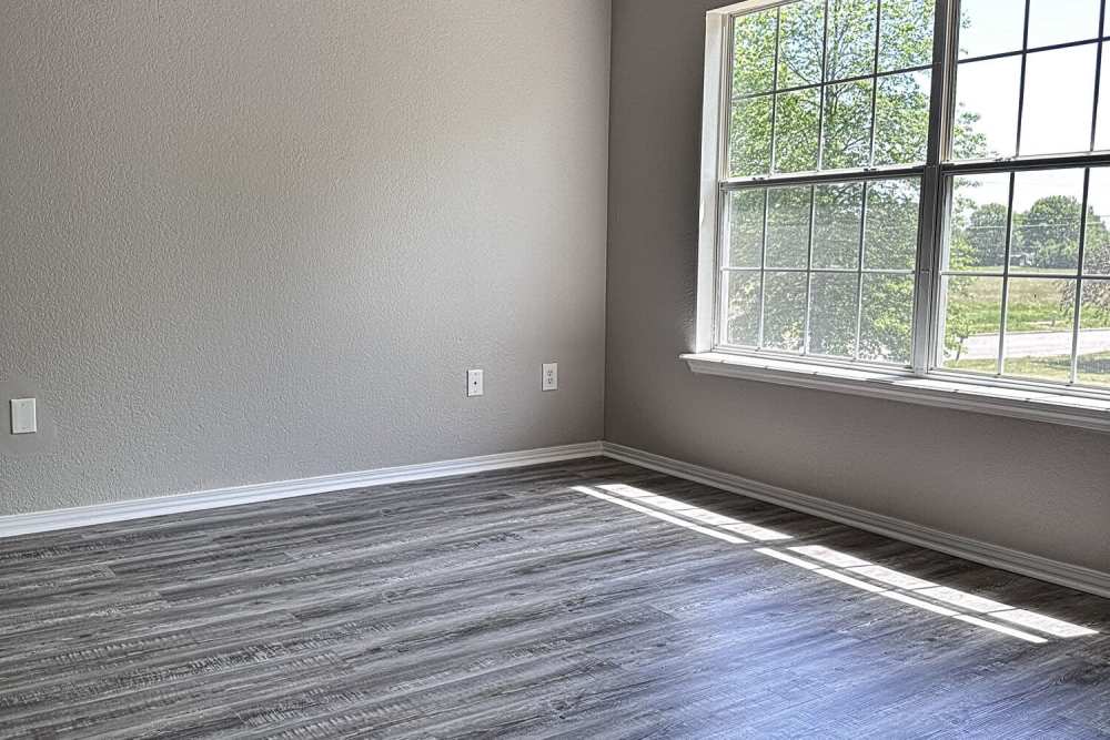 Living area with wood-style flooring and large window at The Gardens At Pryor Creek in Pryor, Oklahoma
