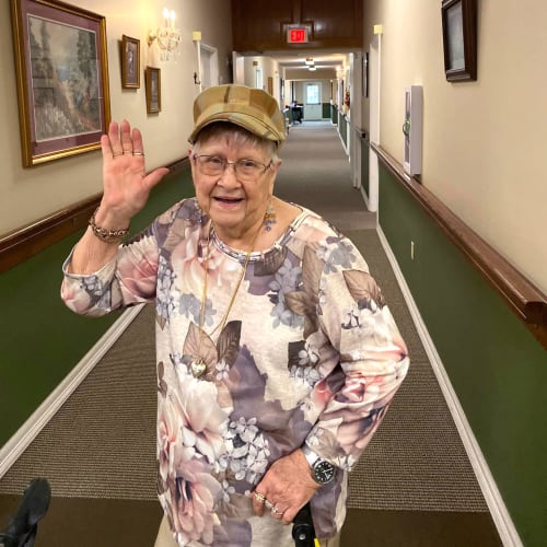 A resident standing in a hallway waving at the camera at Canoe Brook Assisted Living in Duncan, Oklahoma