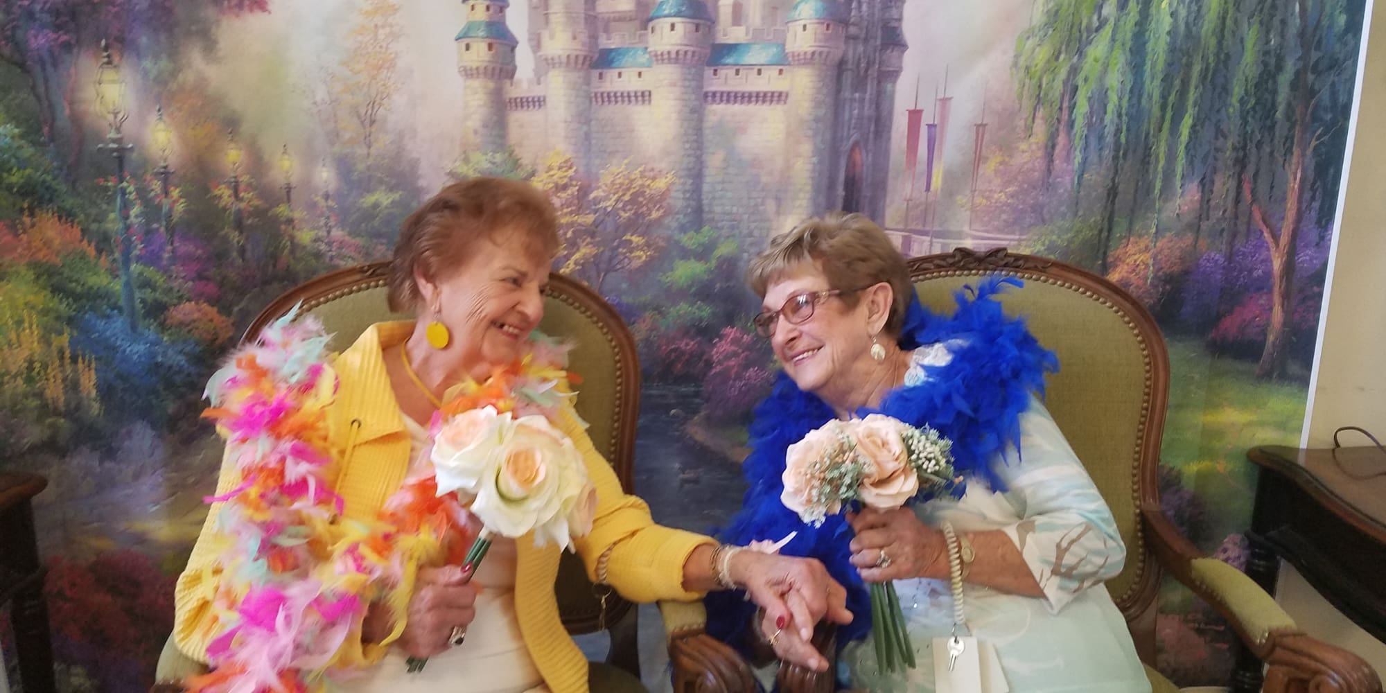 Two happy residents holding hands in front of a castle backdrop at Winterberry Heights Assisted Living and Memory Care in Bangor, Maine