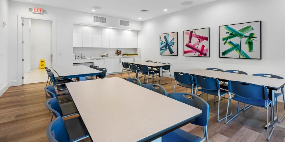 Modern community room with wood-style flooring, tables, and colorful wall art at Solera at Avalon Trails in Delray Beach, Florida