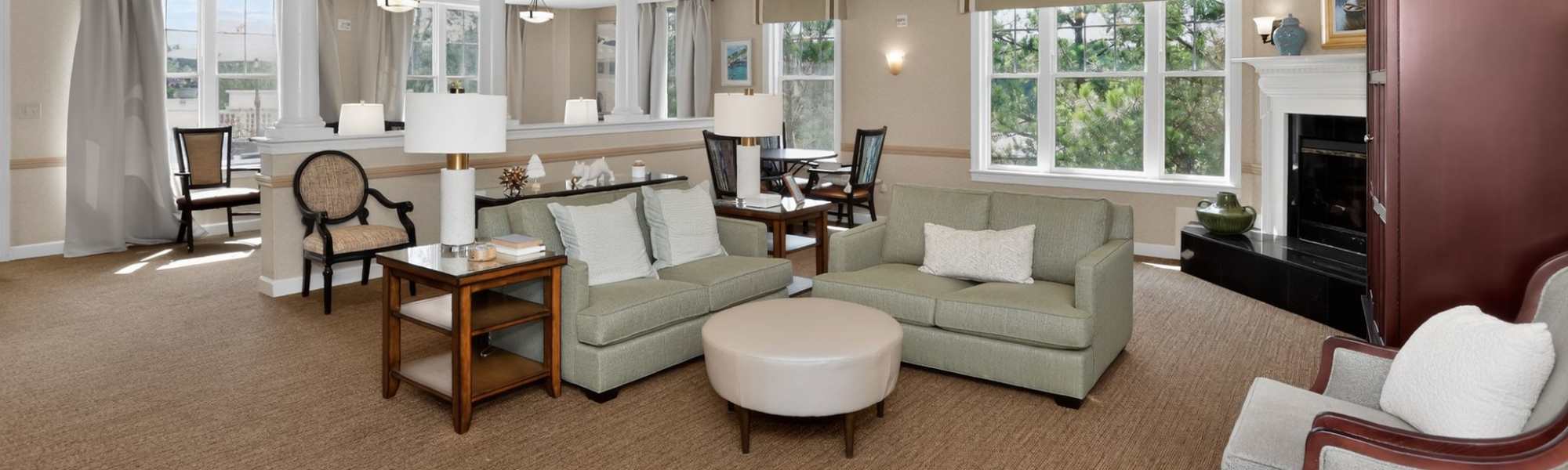 Indoor lounge with sofas, tables, fireplace, and large windows with natural light at Glenncrest at Johns Creek in Johns Creek, Georgia.