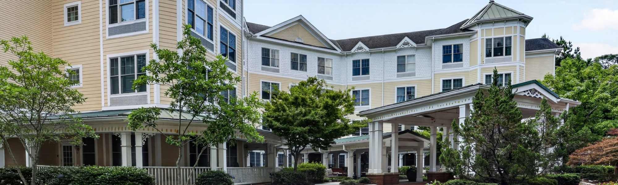 Exterior view of a multi‑story residential building with covered entrance, landscaping, and driveway at Glenncrest at Johns Creek in Johns Creek, Georgia.
