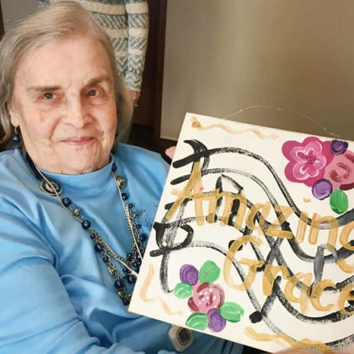 Residents displaying a music-themed painting with the text 'amazing grace' at The Oxford Grand Assisted Living & Memory Care in McKinney, Texas