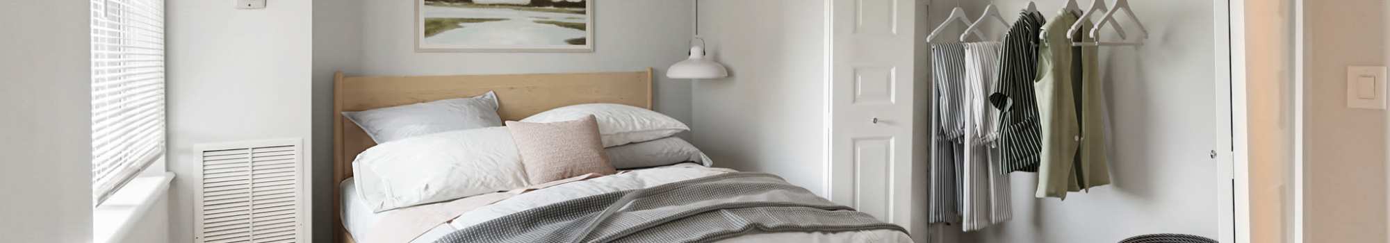 A minimalist bedroom with a wooden bed frame, white bedding, and a striped blue blanket at The Venue in Rochester, New York