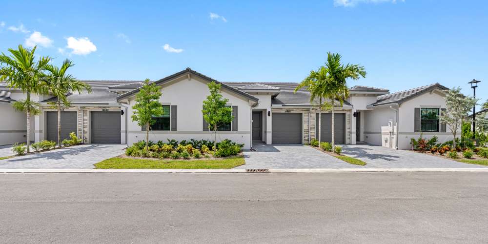 Modern apartment community with landscaped gardens, palm trees, and driveway parking spaces at Solera at Avalon Trails in Delray Beach, Florida