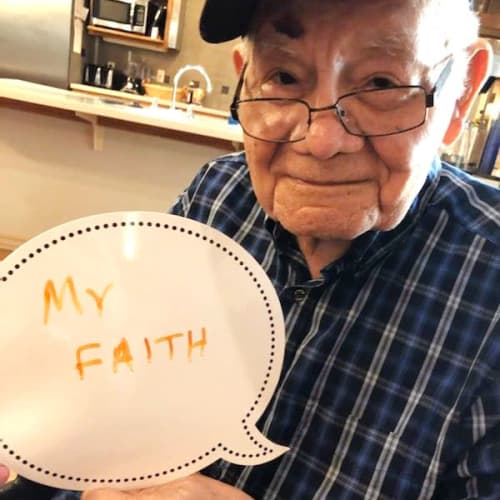 A resident holding a sign that says 'my faith' at Glen Carr House Memory Care in Derby, Kansas