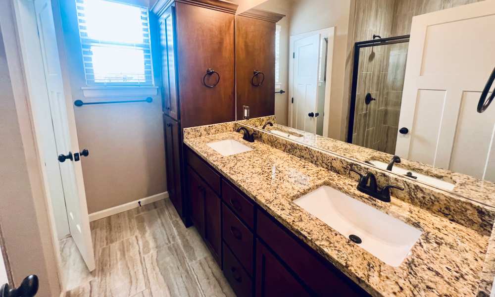 Elegant bathroom featuring a stylish double vanity with granite countertops and a contemporary walk-in shower at Del Norte Duplexes in Yukon, Oklahoma.