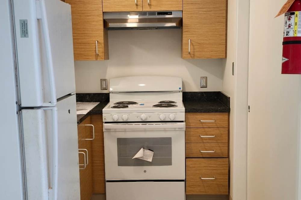 Kitchen and bar with appliances including refrigerator, microwave, oven, and cupboard storage at Kulaimano Elderly Housing in Pepeekeo, Hawaii