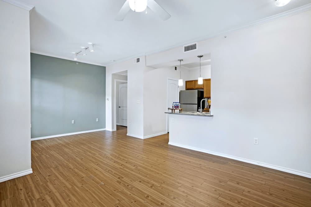 An image capturing the view from the living room area into the dining and kitchen space of an apartment at Cypress Creek at Joshua Station in Joshua, Texas. The apartment features stylish vinyl flooring and a visually appealing accent wall. The open layout creates a seamless transition between the living and dining areas, offering a modern and inviting living space.