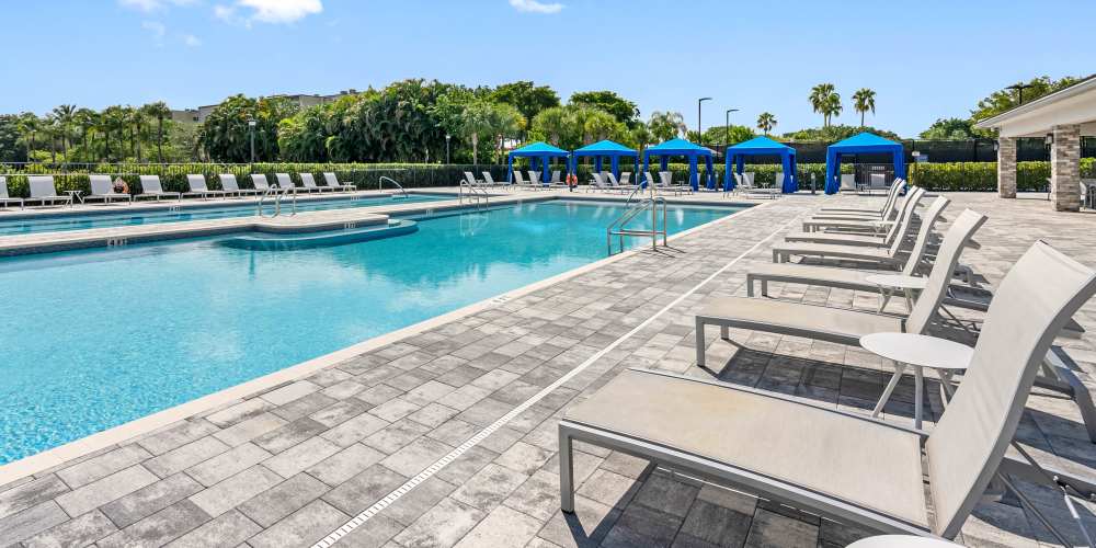 Sparkling resort-style pool with lounge chairs and shaded cabanas surrounded by lush greenery at Solera at Avalon Trails in Delray Beach, Florida