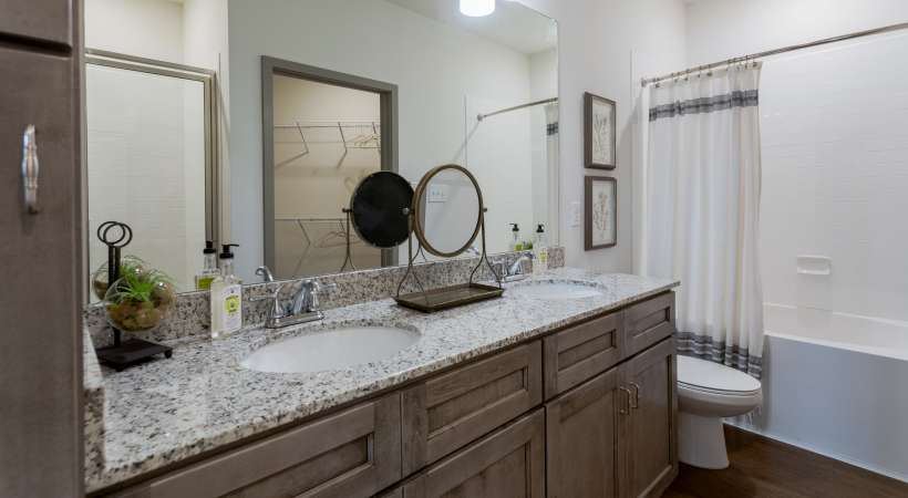 Modern bathroom with double vanity, granite countertop, and large mirror at The Banks at West Fork in Murfreesboro, Tennessee