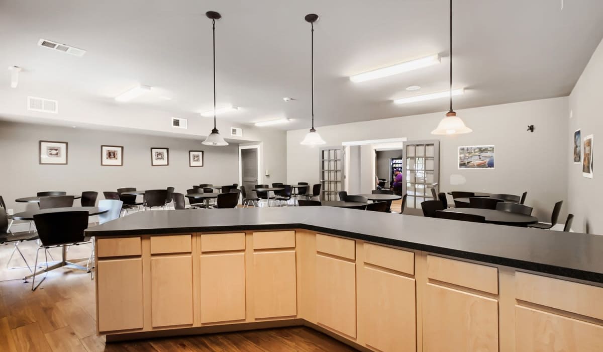 Modern community room with wood-style flooring, tables, chairs, and pendant lighting over a kitchen island at Lindbergh Parc Senior Apartments in Fort Worth, Texas
