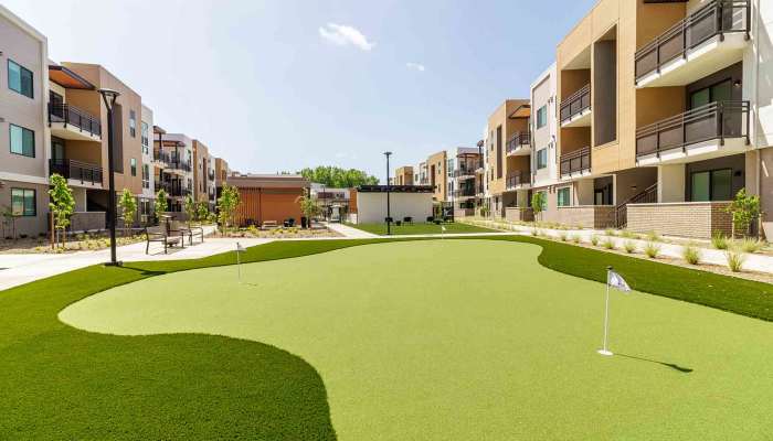 Outdoor putting green surrounded by landscaped areas and apartment buildings at Sutter Green Apartments in Sacramento, California.