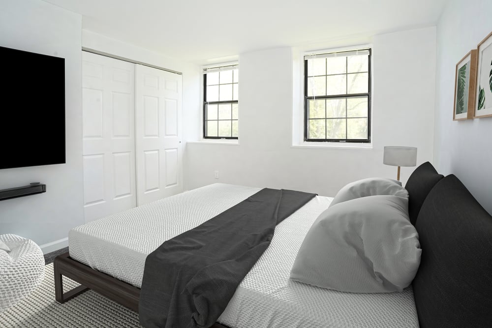Bright bedroom with a queen bed, large windows, and modern decor, featuring a cozy armchair and wall-mounted TV at Dutch Village Apartments in Baltimore, Maryland