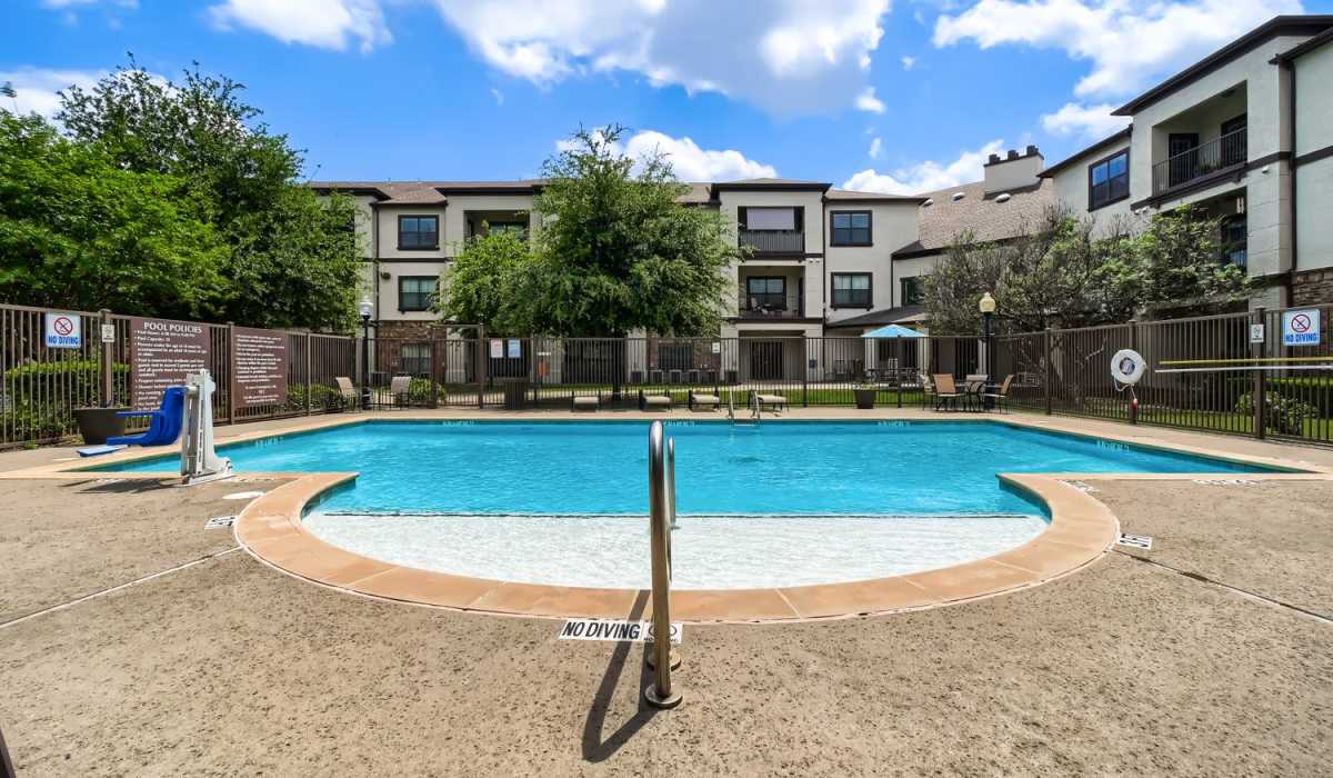 Resort-style sparkling pool with lounge chairs and shaded umbrellas in a landscaped area at Lindbergh Parc Senior Apartments in Fort Worth, Texas