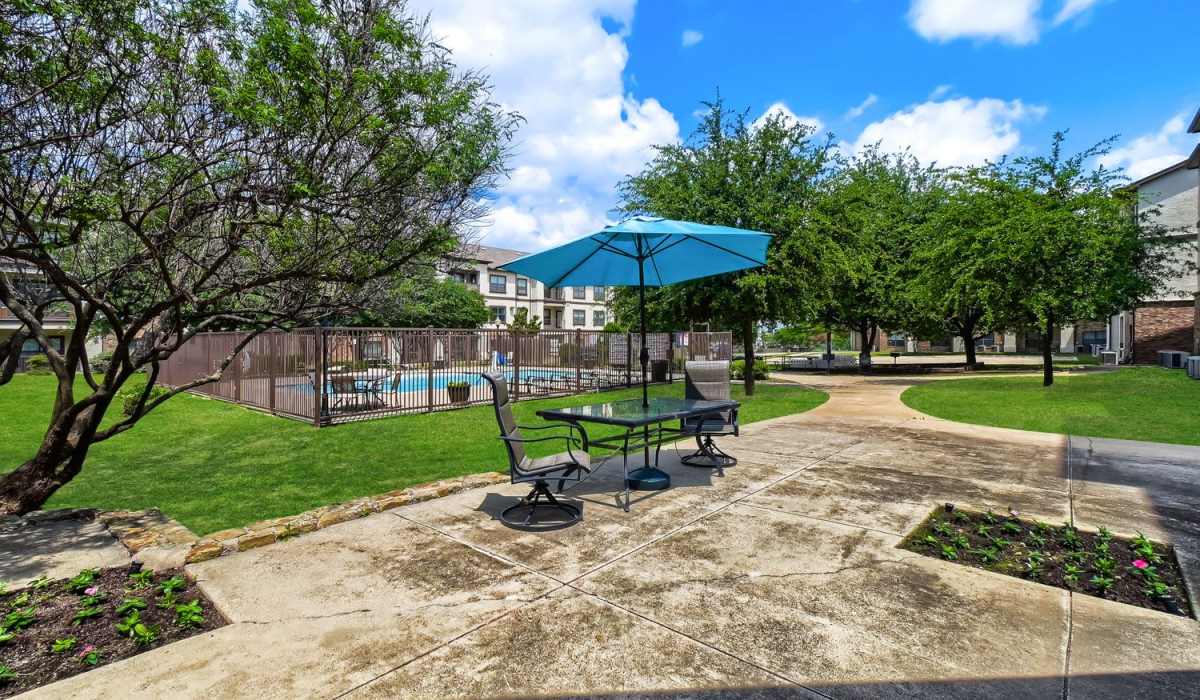 Outdoor seating area with umbrella overlooking a sparkling pool and landscaped green space at Lindbergh Parc Senior Apartments in Fort Worth, Texas
