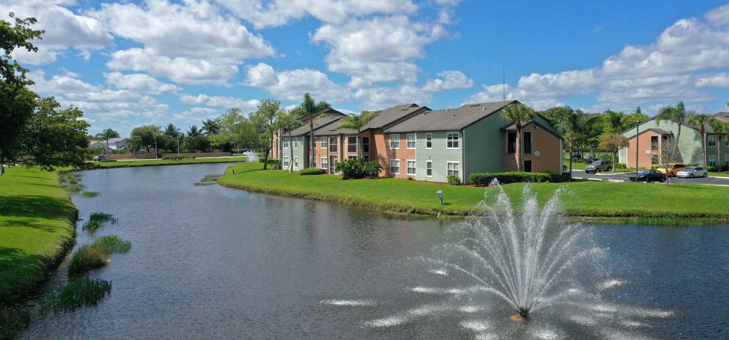 Beautiful view of lake, surrounding green grass and trees right outside apartments at Visions at Willow Pond apartments in West Palm Beach, Florida