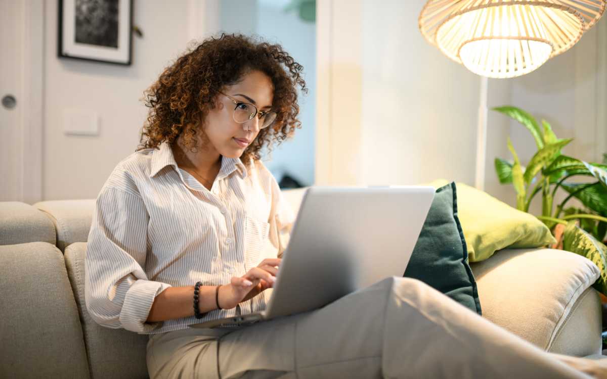 Woman working on laptop while sitting on a cozy sofa with decorative pillows and plants nearby at Fairfield Commons in Stamford, Connecticut 