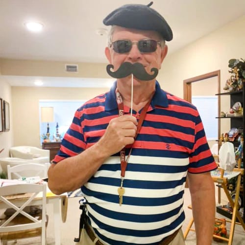 Resident in a beret holding a funny mustache up to their face at The Oxford Grand Assisted Living & Memory Care in McKinney, Texas