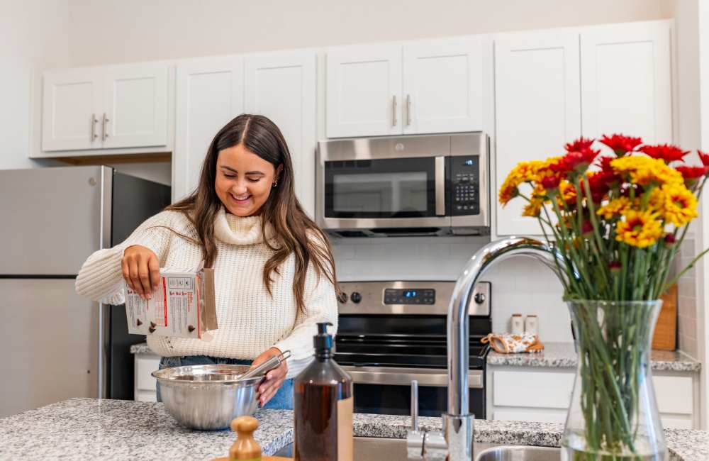Resident woman preparing food in a stainless-steel kitchen at The Waters at Promenade in Marrero, Louisiana