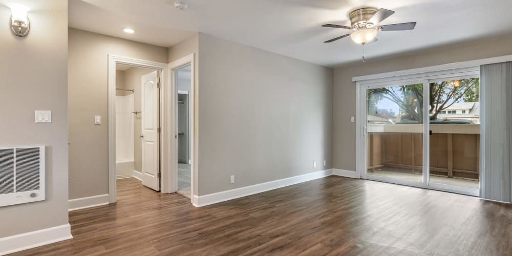 Apartment living room with upgraded light fixtures and wood-style flooring, opening onto a private patio at Pentagon Apartments in Fremont, California