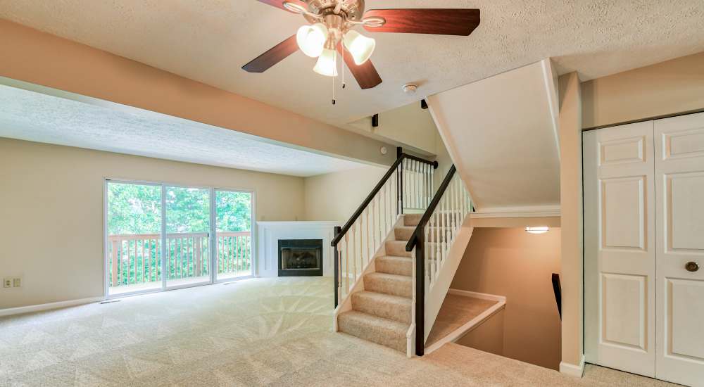 Living room with large windows, ceiling fan and stairs leading to the above floor at Hawthorne Estates in Oakdale, Pennsylvania