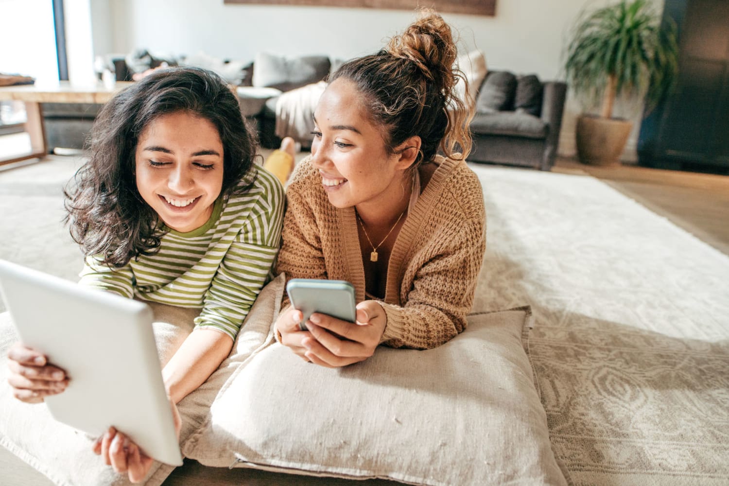 Two friends laying on the ground looking at their tablet and phones at Sterling Park Apartments in Brighton, Colorado