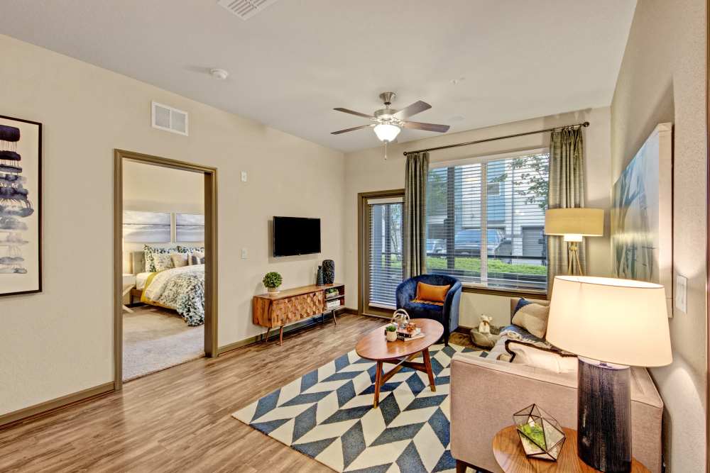 Modern living room with couch, carpet, ceiling fan, large window and wood-style flooring at The Courtney at Lake Shadow in Orlando, Florida 