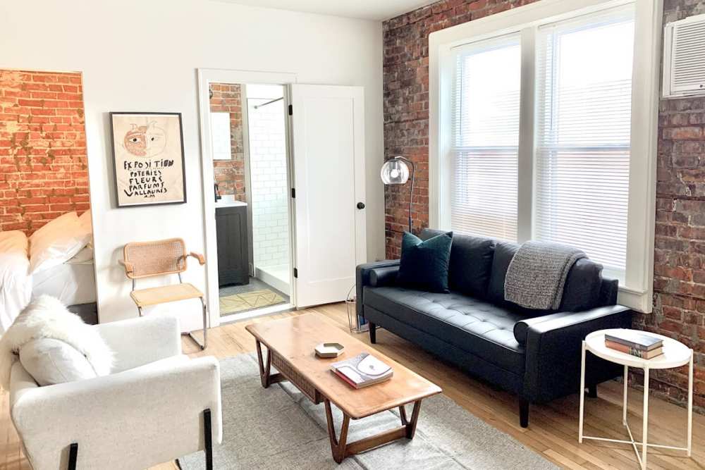 Leather couch and a comfortable chair in a model home's living space with window at Detroit Living in Detroit, 