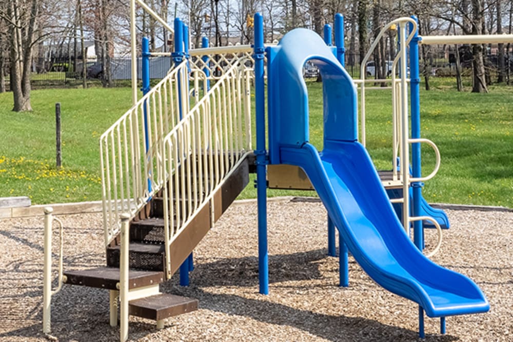 Colorful playground structure with slide and stairs surrounded by green grass and trees at Dutch Village Apartments in Baltimore, Maryland