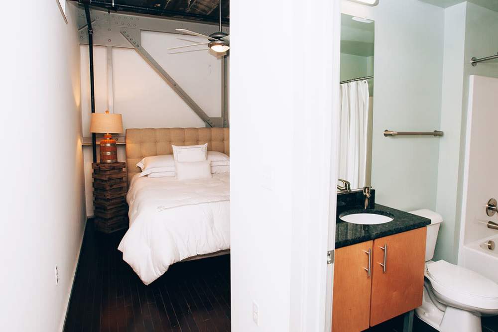 Cozy bedroom with hardwood flooring and ensuite bathroom at Courtyard Lofts at Scott’s Addition in Richmond, Virginia