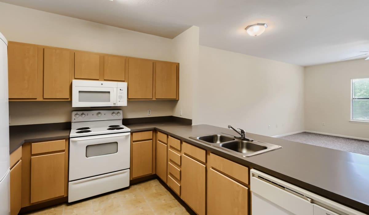 Modern kitchen with wood-style cabinets, white appliances, and ample counter space in open layout at Lindbergh Parc Senior Apartments in Fort Worth, Texas